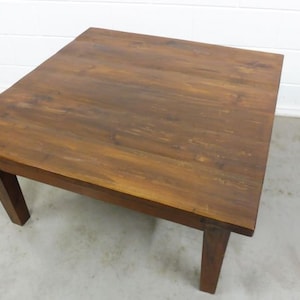 Könnte beinhalten: Ein quadratischer Holz-Couchtisch mit dunkelbrauner Oberfläche. Der Tisch hat ein schlichtes Design mit vier Beinen und einer glatten Tischplatte.