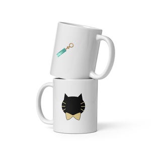 Peut inclure: Deux mugs en céramique blanche empilés. Le mug supérieur présente un motif turquoise et doré. Le mug inférieur présente un visage de chat noir avec un nœud papillon doré. Les deux mugs ont une anse incurvée.