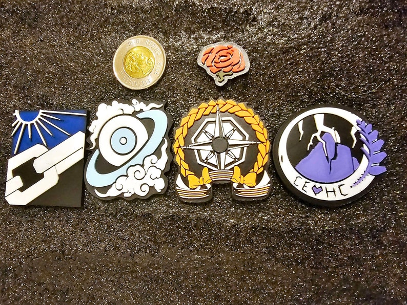 May include: Six colourful embroidered patches with various designs, including a sun, a chain, a planet, a compass, a mountain, and a rose. The patches are on a dark grey textured background.