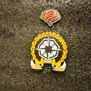 May include: A black and white compass design with a yellow wreath and two yellow bows. The compass is surrounded by a black background. A red rose is in the top centre of the image.