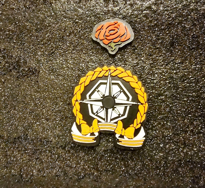 May include: A black and white compass design with a yellow wreath and two yellow bows. The compass is surrounded by a black background. A red rose is in the top centre of the image.