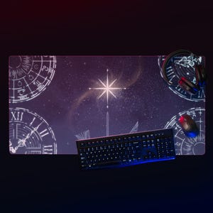 May include: A rectangular desk mat with a celestial design featuring a starry night sky, zodiac symbols, and a central starburst. A black keyboard, mouse, and headset are on the mat.