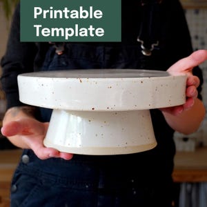 以下が含まれることがあります： 白い陶器のケーキスタンド。まだら模様のデザイン。スタンドは幅広で平らな上面と台座ベースを備えています。「Printable Template」の文字が左上の緑色の長方形にあります。