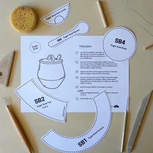 May include: A craft project with paper templates for a sugar bowl, including a base, top, and spoon. A sponge and tools are also present. The instructions are printed on a white sheet.