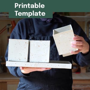 Op de afbeelding: Drie gebroken witte vierkante keramische bakjes met bruine spikkels, twee rustend op een rechthoekig dienblad en één apart vastgehouden. De tekst Printable Template staat in het wit op een donkergroene achtergrond bovenaan de afbeelding.