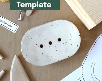 May include: A speckled, off-white ceramic soap dish with three drainage holes. The oval-shaped dish is surrounded by craft supplies and a green banner that reads "Printable Template".