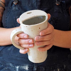 K&ouml;nnte beinhalten: Eine wei&szlig;e Keramiktasse mit braunen Flecken und einem einzigartigen Ausschnitt-Design. Die Tasse hat einen Henkel und eine breite &Ouml;ffnung.