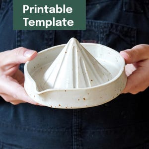 Könnte beinhalten: Handgefertigte Zitruspresse aus Keramik mit konischem Reibkopf und einer breiten, flachen Schüssel. Die Zitruspresse ist cremefarben mit braunen Sprenkeln und einem Ausguss. Der Text "Printable Template" befindet sich in einem grünen Rechteck.