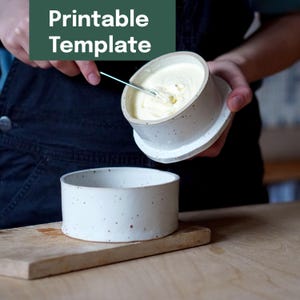 May include: A white ceramic butter dish with a lid, filled with butter, and a matching base. The dish is speckled with brown dots. The text "Printable Template" is in a green rectangle in the upper left corner.
