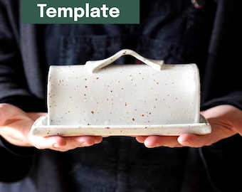 May include: A white ceramic butter dish with brown speckles, held in both hands. The dish has a rectangular base and a curved lid with a handle. The words "Printable Template" are in a green rectangle above.