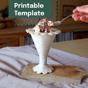May include: A white ceramic sundae dish with a scalloped rim, filled with ice cream, chocolate sauce, and sprinkles. The dish sits on a wooden cutting board. The text "Printable Template" is in a green box in the upper left corner.