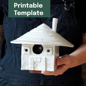 Peut inclure: Une maison d'oiseau en céramique blanche avec une cheminée et un toit en pointe. La maison d'oiseau a une ouverture ronde et des fenêtres carrées. Le texte "Printable Template" est dans un rectangle vert au-dessus.