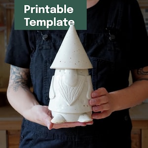 Könnte beinhalten: Eine weiße Keramik-Gnomfigur mit einem konischen Hut, die eine gesprenkelte Textur und einen geformten Bart aufweist. Der Gnom hat einen glatten, abgerundeten Körper und einen spitzen Hut. Der Text "Printable Template" steht in einem grünen Kasten.