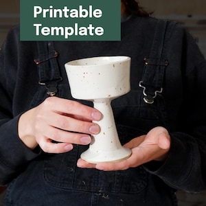 May include: A handmade, off-white ceramic goblet with a speckled finish. The goblet has a wide, shallow bowl and a flared, pedestal base. The text "Printable Template" is in a dark green rectangle in the upper left corner.
