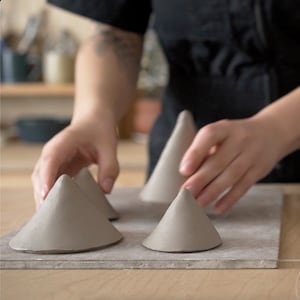 May include: Five grey ceramic cones arranged on a grey surface. The cones are different sizes and are arranged in a staggered pattern.