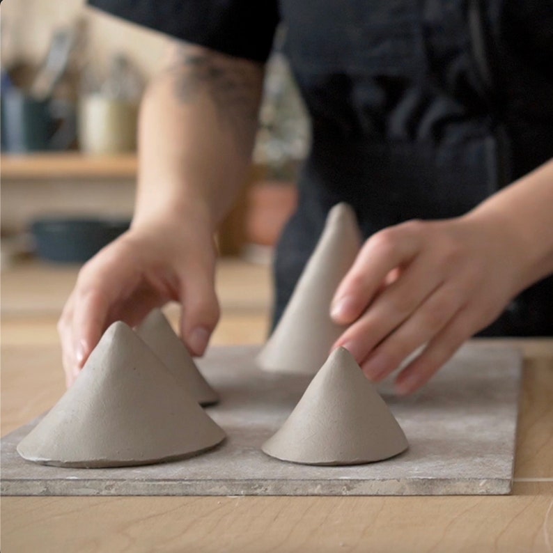 May include: Five grey ceramic cones arranged on a grey surface. The cones are different sizes and are arranged in a staggered pattern.
