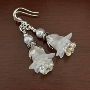May include: A pair of silver earrings with white frosted flower charms and pearl beads.