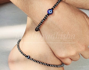 May include: A black beaded bracelet and anklet with a blue evil eye charm. The bracelet and anklet are made of small black beads with silver accents.