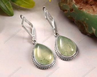 May include: A pair of silver dangle earrings with green teardrop-shaped stones. The stones have a translucent, cloudy appearance.
