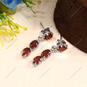 Peut inclure: Une paire de boucles d'oreilles pendantes en argent avec trois pierres précieuses ovales rouges. Les boucles d'oreilles ont un design délicat avec une petite perle d'argent au sommet de chaque boucle d'oreille.