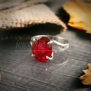 May include: A silver ring with a large, oval-shaped, red gemstone. The ring has a delicate, open design.