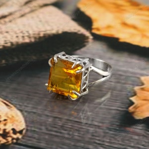 May include: A silver ring featuring a large, square-shaped, yellow gemstone set in a filigree design.