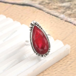 May include: A silver ring featuring a teardrop-shaped red gemstone set in a silver bezel. The ring has a decorative band with small silver beads.