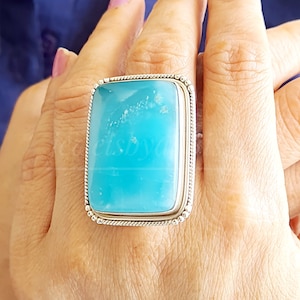 May include: A silver ring with a large, rectangular, light blue gemstone. The ring is set in a silver band with a beaded edge.