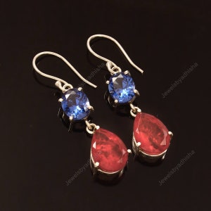 May include: A pair of silver dangle earrings with blue and red gemstones. The top gemstone is a round blue stone, and the bottom gemstone is a teardrop-shaped red stone.