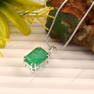 May include: A silver chain necklace with a pendant featuring a large, emerald green gemstone set in a silver frame.