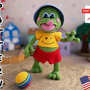 Peut inclure: Patron de crochet pour une grenouille verte portant un chapeau bleu, une chemise jaune et un short rouge. La grenouille tient un ballon coloré. Le patron est disponible en téléchargement PDF.
