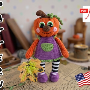 Op de afbeelding: Haakpatroon voor een pompoenvormige amigurumi-pop met een paarse jurk, zwart-wit gestreepte leggings en paarse schoenen. De pop heeft een vriendelijk gezicht met grote ogen en een kleine neus. Het patroon is beschikbaar als PDF-download.