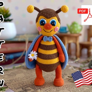 May include: A handmade crochet bee doll with a smiling face, blue eyes, and a blue bow tie. The bee has brown and yellow striped body, orange legs, and blue wings. The word "PATTERN" is written vertically on the left side of the image.