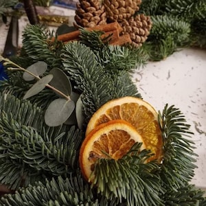 May include: A festive Christmas wreath featuring fresh fir branches, dried orange slices, cinnamon sticks, and pine cones. This natural wreath is a rustic decoration for the holiday season.