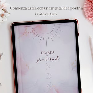 Pu&ograve; includere: Un tablet digitale rosa e bianco con una cornice color oro rosa. Lo schermo mostra uno sfondo acquerellato rosa e bianco con un design di sole e luna. Il testo "DIARIO de gratitud" &egrave; scritto in corsivo sullo schermo. Il testo "Comienza tu dia con una mentalidad positiva" &egrave; scritto sopra il tablet. Il testo "Gratitud Diaria" &egrave; scritto sotto il tablet.