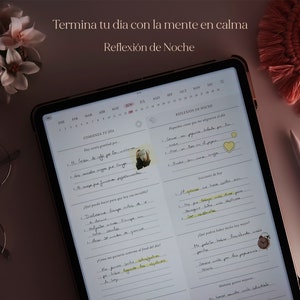 Pu&ograve; includere: Un planner digitale aperto su una pagina con un calendario e una sezione intitolata "Comienza Tu D&iacute;a" e "Reflexi&oacute;n de Noche". Il planner &egrave; su una superficie rosa chiaro con un fiocco rosa e un paio di occhiali.