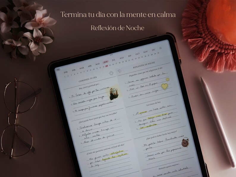 Pu&ograve; includere: Un planner digitale aperto su una pagina con un calendario e una sezione intitolata "Comienza Tu D&iacute;a" e "Reflexi&oacute;n de Noche". Il planner &egrave; su una superficie rosa chiaro con un fiocco rosa e un paio di occhiali.