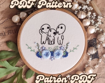 May include: A white embroidery hoop with a black and white embroidery design of three small figures with blue flowers. The text "PDF Pattern" is in the top left corner and "Patrón PDF" is in the bottom right corner.