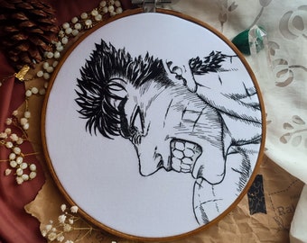 May include: Hand-stitched embroidery art on white fabric, depicting a black and white illustration of a character with an angry expression. The artwork is framed in a wooden embroidery hoop. The background includes decorative elements.