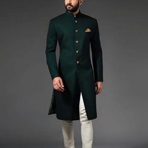 Puede incluir: Un sherwani de color verde oscuro con cuello mao, mangas largas y una tapeta frontal con botones dorados. Un pequeño pañuelo de bolsillo dorado se encuentra en el bolsillo del pecho. El conjunto se combina con pantalones ajustados color crema.