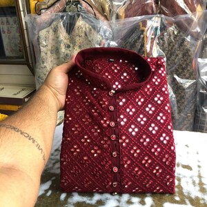 Puede incluir: Una kurta de color granate con cuello mandar&iacute;n y cierre de bot&oacute;n. La kurta est&aacute; decorada con peque&ntilde;os espejos redondos y un patr&oacute;n geom&eacute;trico.