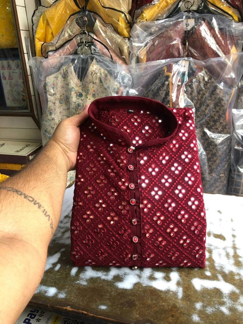 Puede incluir: Una kurta de color granate con cuello mandar&iacute;n y cierre de bot&oacute;n. La kurta est&aacute; decorada con peque&ntilde;os espejos redondos y un patr&oacute;n geom&eacute;trico.