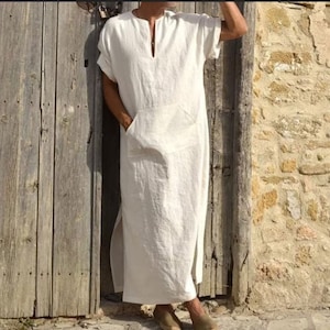 Peut inclure: Une kaftan en lin blanc avec un col en V et une seule poche sur le devant. La kaftan a des fentes latérales et des manches courtes.