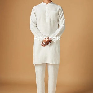 Puede incluir: Una kurta de lino blanco con cuello abotonado y un solo bolsillo en el pecho. La kurta se lleva con pantalones de lino blanco y sandalias de cuero marr&oacute;n. El texto "Achichpalette ACP" est&aacute; impreso en la parte delantera de la kurta.