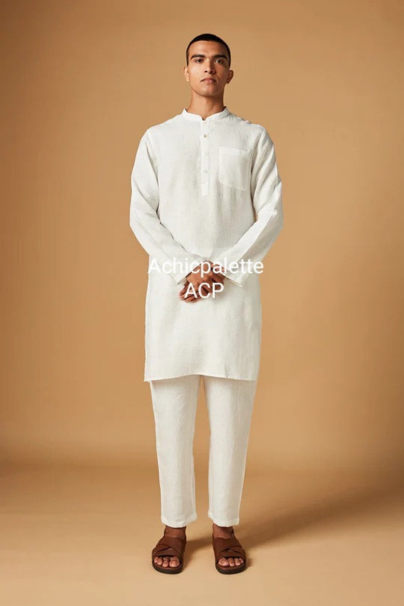 Puede incluir: Una kurta de lino blanco con cuello abotonado y un solo bolsillo en el pecho. La kurta se lleva con pantalones de lino blanco y sandalias de cuero marr&oacute;n. El texto "Achichpalette ACP" est&aacute; impreso en la parte delantera de la kurta.