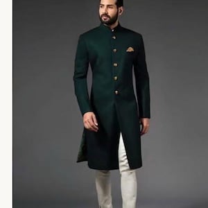Peut inclure: Une veste sherwani vert fonc&eacute; arrivant au genou avec un col officier, des manches longues et une patte de boutonnage frontale orn&eacute;e de boutons dor&eacute;s. Une pochette dor&eacute;e est ins&eacute;r&eacute;e dans la poche poitrine gauche. Port&eacute;e avec un pantalon blanc cass&eacute;.