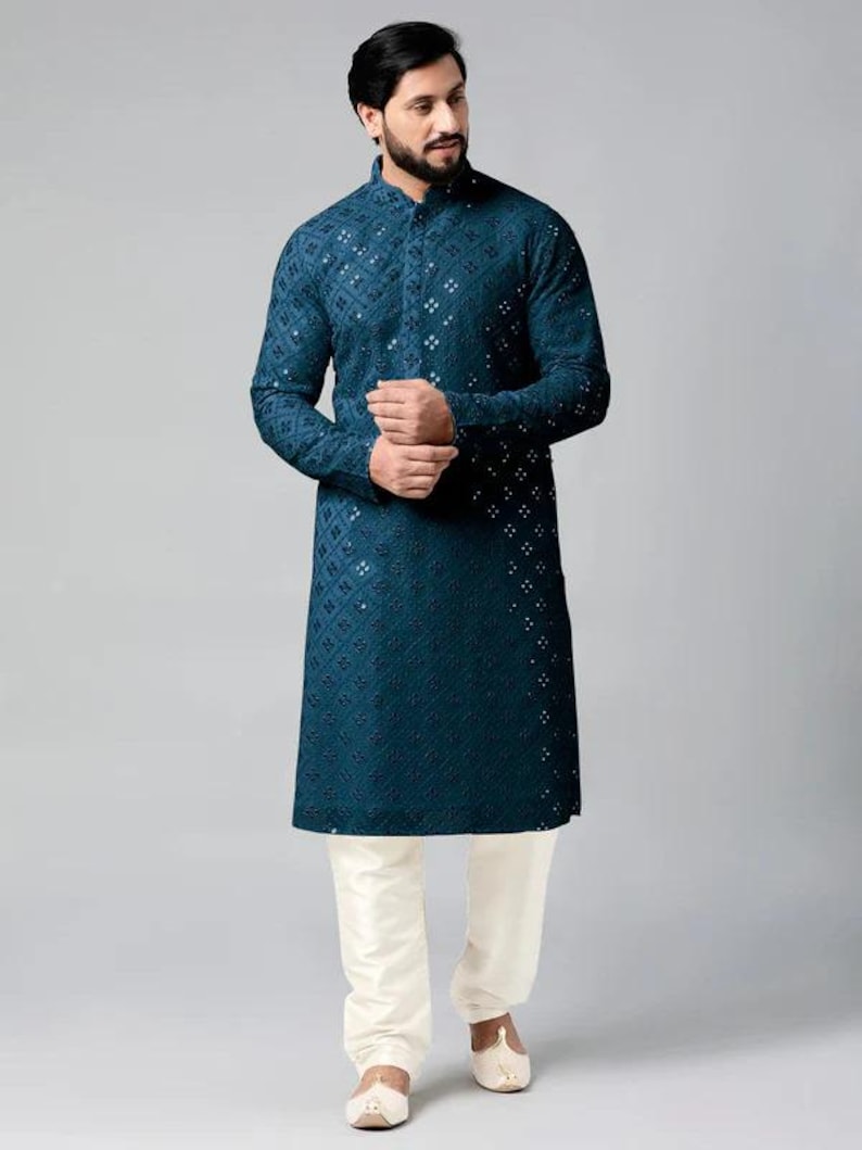 Puede incluir: Una kurta azul turquesa con cuello blanco abotonado y un patr&oacute;n geom&eacute;trico. La kurta es de manga larga y tiene un corte recto. El modelo lleva pantalones blancos y zapatos blancos.