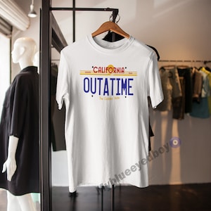 May include: White t-shirt featuring a graphic of a California license plate that reads "OUTATIME" with the words "The Golden State" underneath.