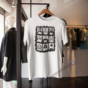 May include: White t-shirt with a black and white graphic of horror film characters presented as mugshots. Each character is in a box with a number beneath. The tee is displayed on a wooden hanger.