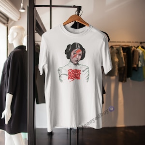 May include: White t-shirt featuring a graphic of Princess Leia from Star Wars with a lightning bolt across her eye and the words "Rebel Rebel" in red.